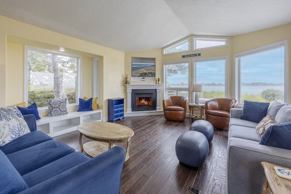 A spacious living room with a fireplace, large windows, and a view of the outdoors.