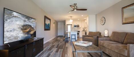 A modern living room with a flat-screen TV, a ceiling fan, and a wooden coffee table.