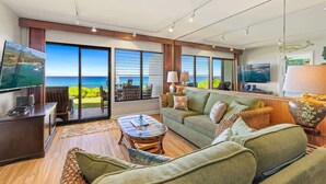 Un salón espacioso con un gran ventanal con vistas al océano, un sofá cómodo, una mesa de centro y un televisor.