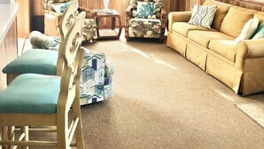Ein gemütliches Wohnzimmer mit Deckenventilator, einem beigefarbenen Sofa, zwei Sesseln und einem Couchtisch.