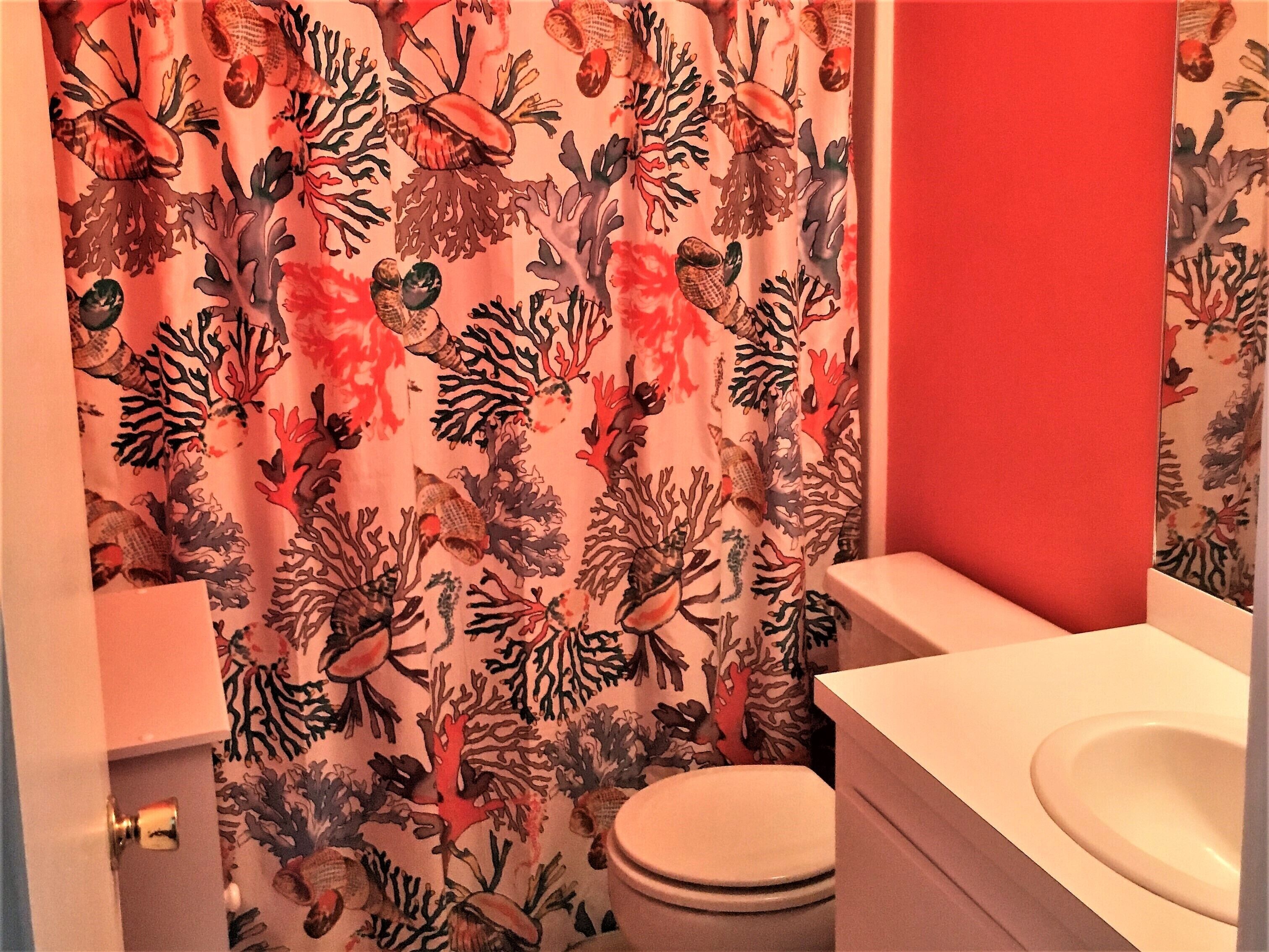 Un baño con cortina de ducha con estampado de arrecife de coral, un inodoro blanco y un lavabo blanco.