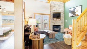 A cozy living room with a stone fireplace, a comfortable sofa, a coffee table, and a TV mounted on the wall. - Pikes Peak Ranch - Eagle Crest Cabin (Woodland Park)