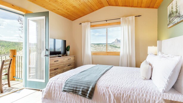 A bedroom with a bed, a TV, a dresser, and a window with a view of the mountains. - Pikes Peak Ranch - Eagle Crest Cabin (Woodland Park)