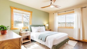 A bedroom with a bed, bedside tables, a ceiling fan, and large windows with curtains. - Pikes Peak Ranch - Eagle Crest Cabin (Woodland Park)