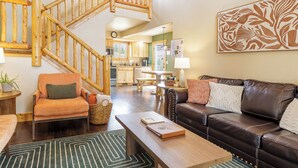 A spacious living area with a wooden staircase, a leather sofa, a dining table, and a kitchen in the background. - Pikes Peak Ranch - Eagle Crest Cabin (Woodland Park)