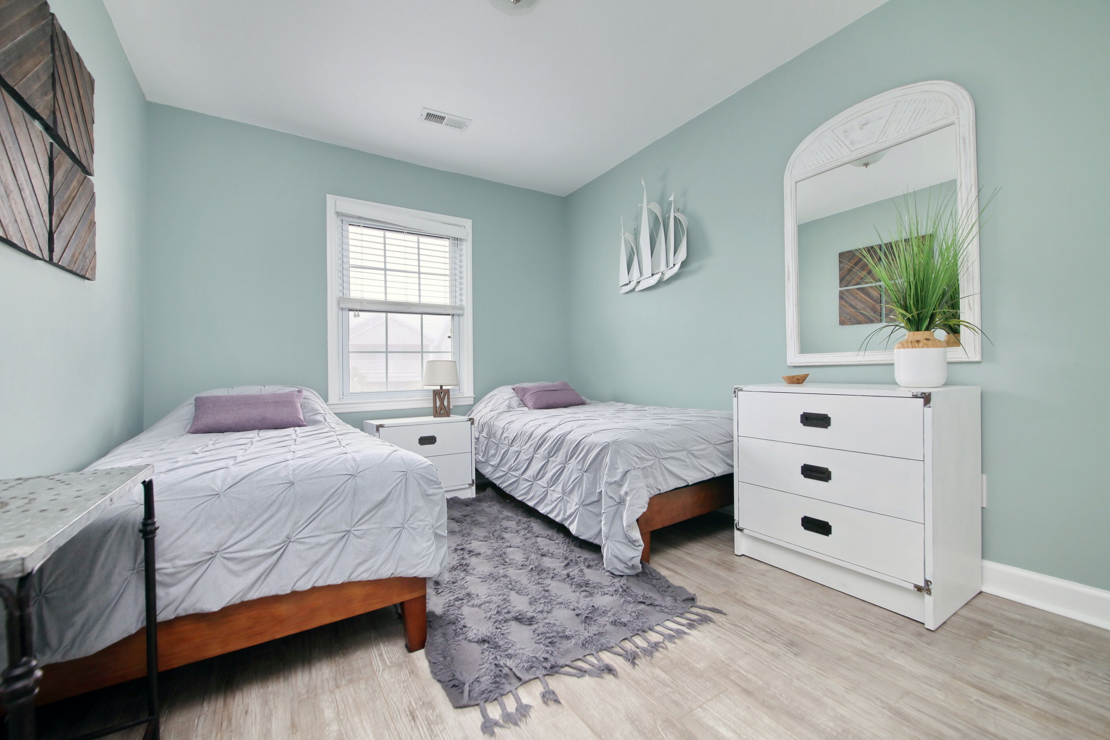 A bedroom with two beds, a dresser, a window, and a mirror.