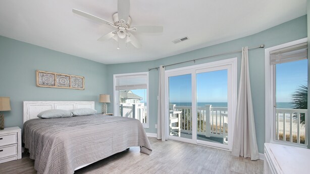 A bedroom with a bed, a ceiling fan, and a view of the ocean through large windows. - OCEANFRONT TH with pool on the beach! (Surfside Beach)