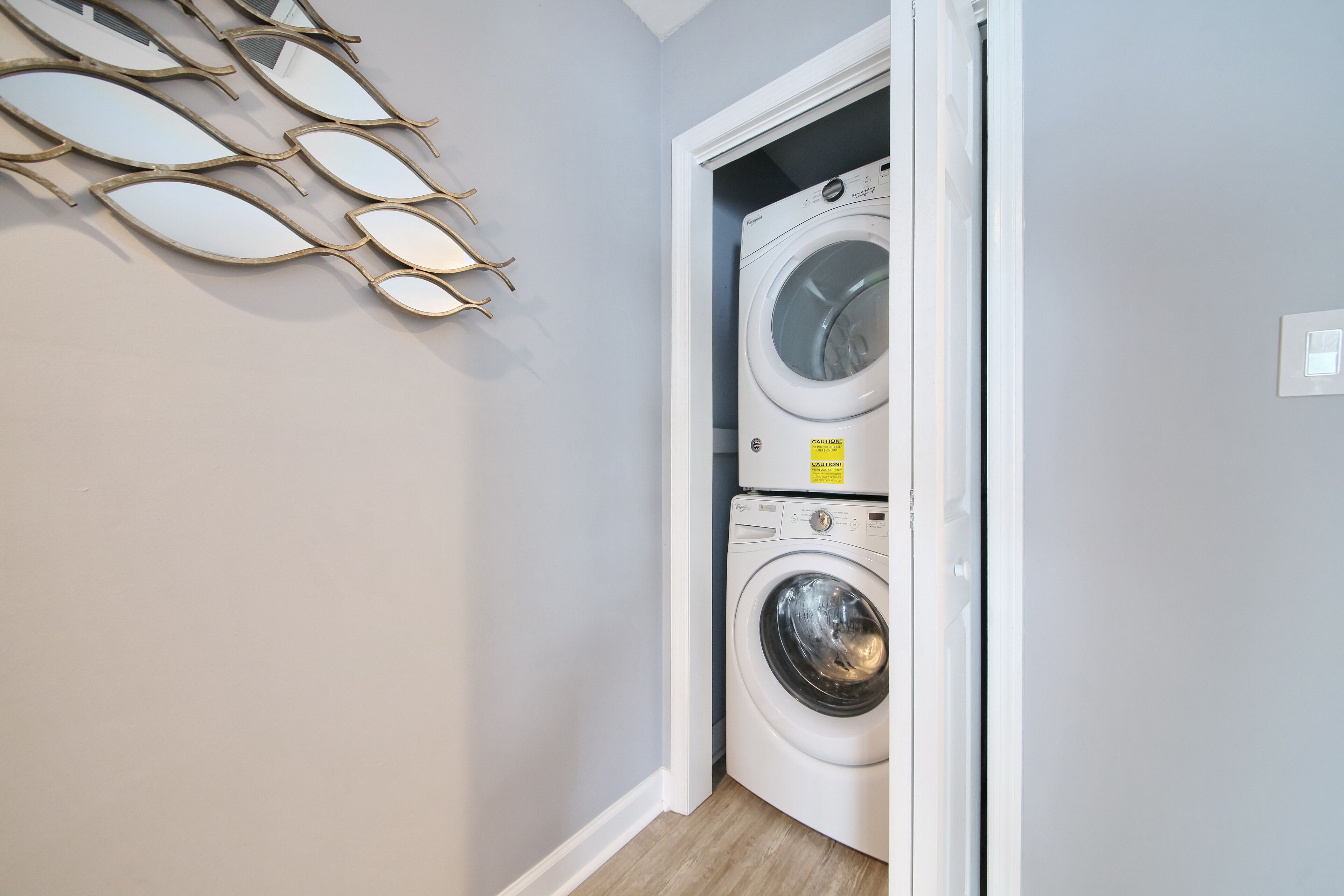 A laundry room with a washing machine and dryer, a wall-mounted towel rack, and a caution sign on the dryer.