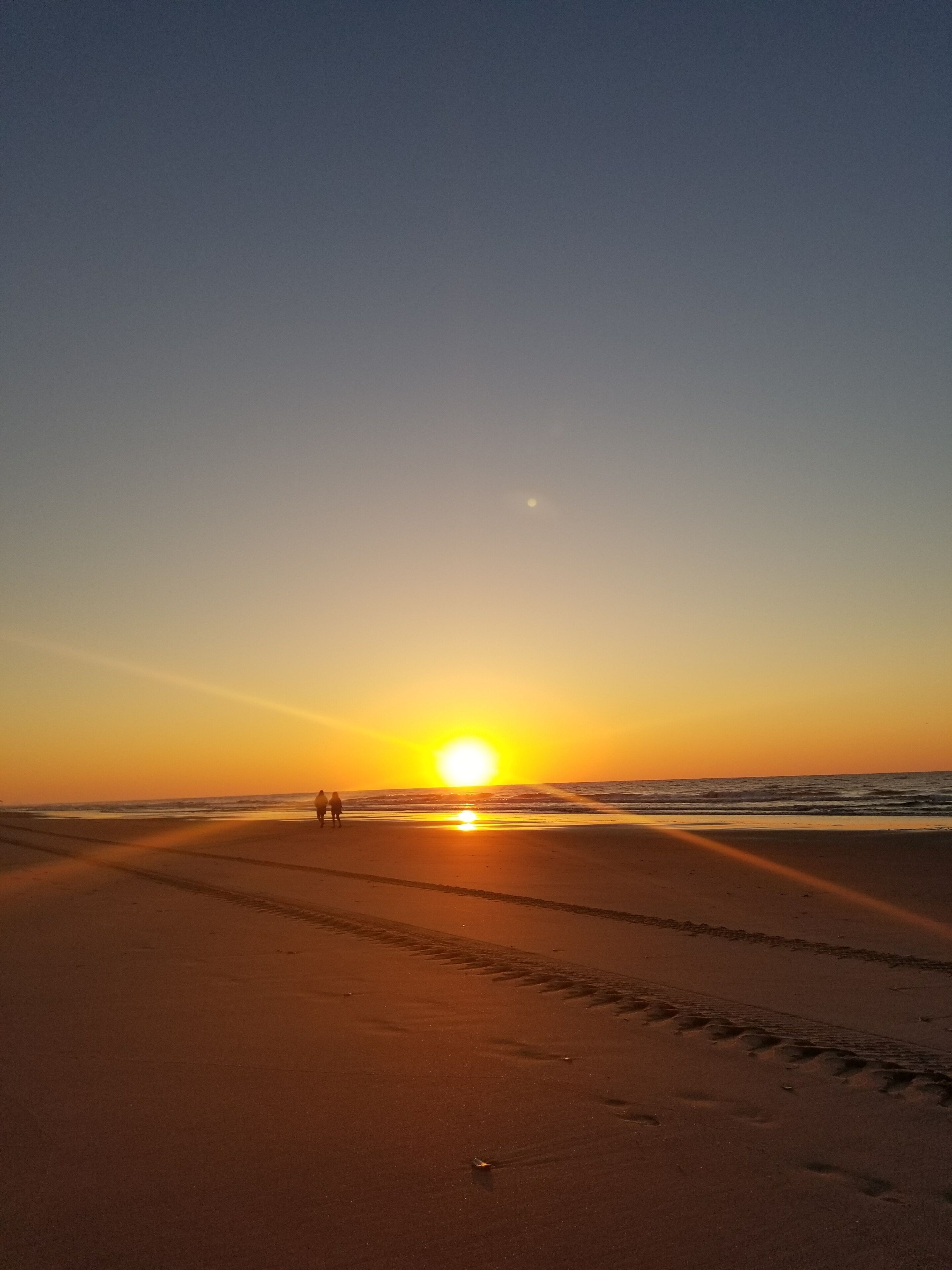 A beach scene at sunset with footprints leading towards the ocean.