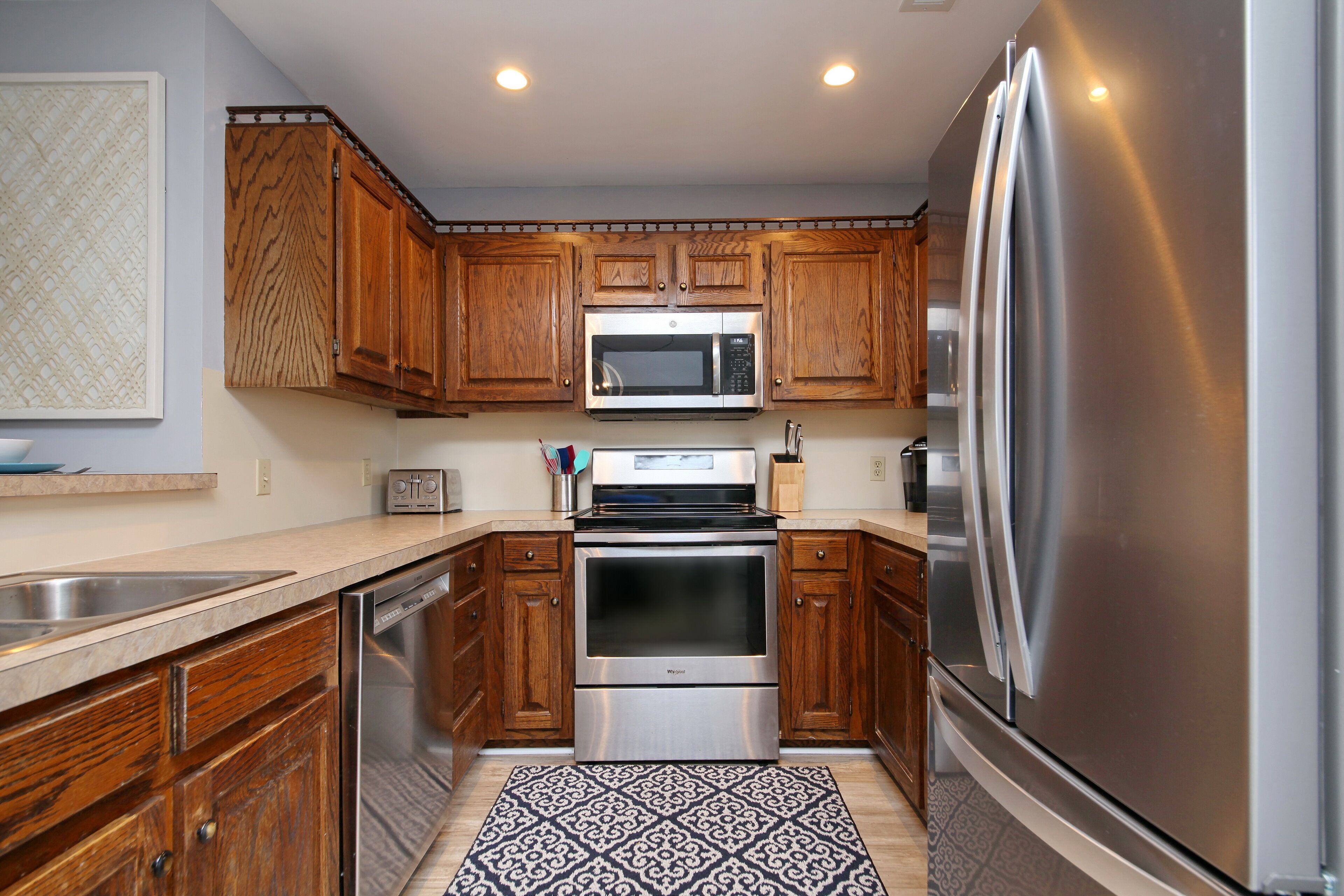 A modern kitchen with wooden cabinets, stainless steel appliances, and a patterned rug.