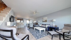 A spacious living room with a high ceiling fan, a staircase on the left, and a dining area in the background. - OCEANFRONT TH with pool on the beach! (Surfside Beach)