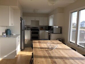 Een moderne keuken met witte kastjes, roestvrijstalen apparatuur en een houten eettafel.