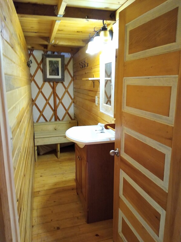 A wooden cabin bathroom with a wooden bench, a sink, and a mirror. - Eagle Yurt at Wilderness Wind, Ely, MN with 3 bedrooms and full kitchen (Ely)