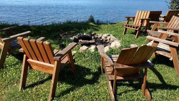 Un cadre idyllique au bord du lac, avec des chaises en bois disposées autour d’un foyer.