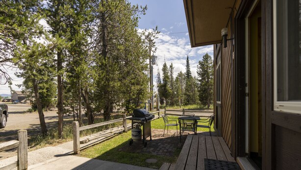 A wooden deck with a grill and outdoor seating, surrounded by trees and a clear sky.