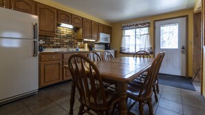 A kitchen with wooden cabinets, a refrigerator, a microwave, and a dining table with chairs.