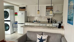 Un espacio habitable compacto con kitchenette, un sofá gris con un cojín de estrella de mar y una zona de lavandería con lavadora y secadora.
