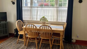Un comedor con una mesa, cuatro sillas, un florero con flores y un televisor sobre un mueble.