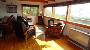 A cozy living room with a piano, leather chairs, a patterned sofa, and large windows offering a view of greenery. - Musician's Paradise With Spectacular Views (Homer)