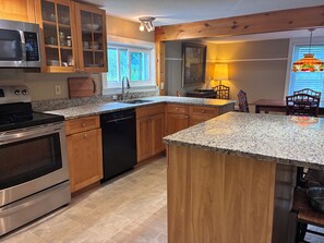 A kitchen with granite countertops, wooden cabinets, stainless steel appliances, and a window with a view.