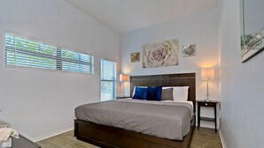 A bedroom with a large bed, two bedside tables, a nightstand, and a window with blinds.