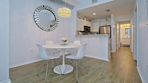 A modern kitchen with stainless steel appliances, a dining area with a round table and white chairs, and a decorative mirror on the wall.