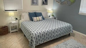 Un dormitorio con cama, mesitas de noche, lámpara, decoración en la pared y ventana con persianas.