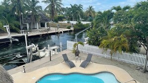Una piscina con valla blanca y sillones de descanso, rodeada de palmeras y un muelle.