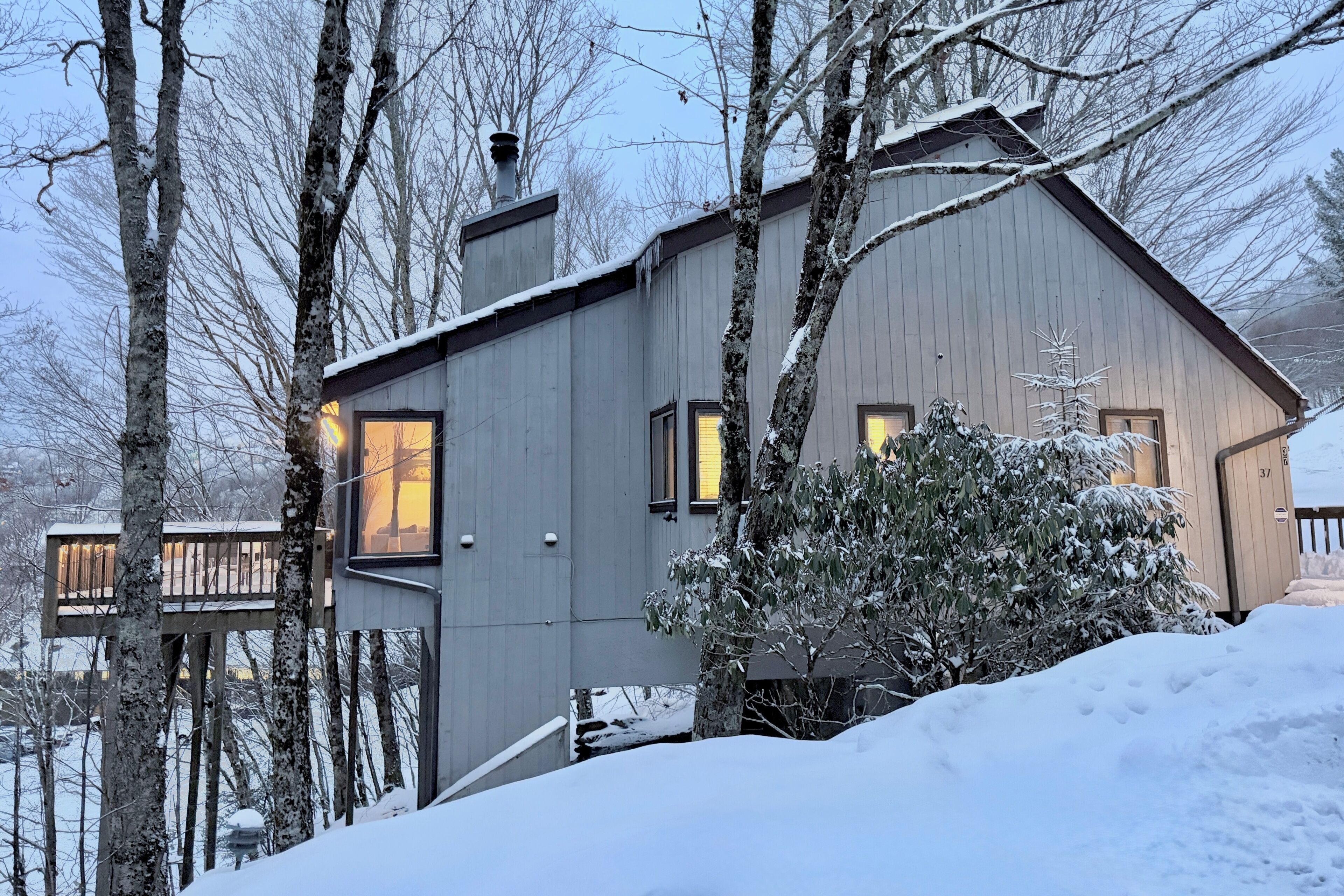 Ett modernt hus med en veranda, omgivet av snötäckta träd och ett snöigt landskap.