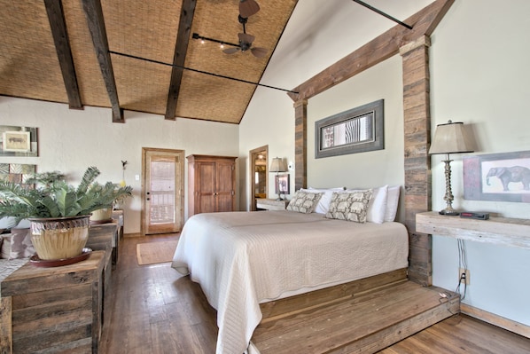 A spacious bedroom with a large bed, wooden beams, and a ceiling fan.