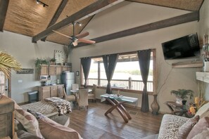 A spacious room with a wooden ceiling, a ceiling fan, a television mounted on the wall, a dining table with chairs, a sofa, and a bed with a zebra print blanket.