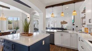 A modern kitchen with white cabinetry, a central island, pendant lighting, and a view to the dining area.