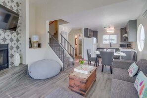 Uma sala de estar moderna com sofá, mesa de centro, puff, escada e área de cozinha.