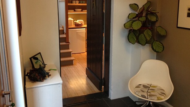 A hallway leading to a kitchen with a dark door, a white chair, and a potted plant. - Charming Renovated 19th-century Coach House (EDINBURGH)