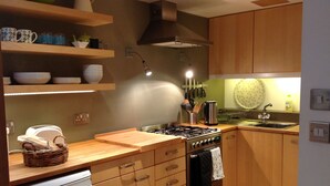 A modern kitchen with wooden cabinets, a gas stove, a sink, and a dish rack. - Charming Renovated 19th-century Coach House (EDINBURGH)