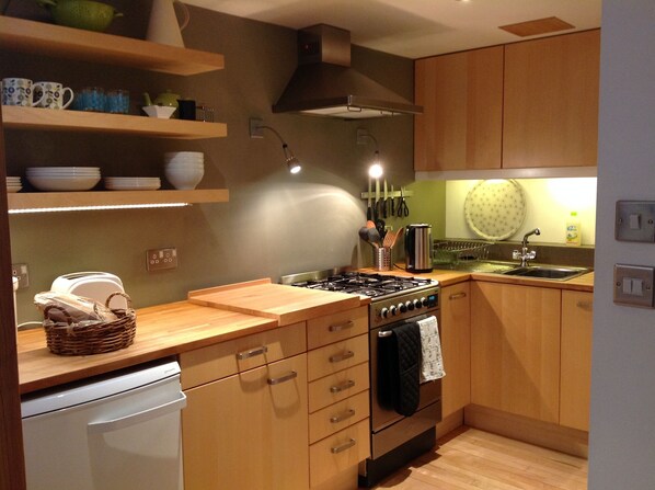 A modern kitchen with wooden cabinets, a gas stove, a sink, and a dish rack.