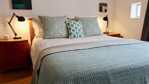 A neatly made bed with patterned pillows, a bedside lamp, and a clock on a wooden nightstand. - Charming Renovated 19th-century Coach House (EDINBURGH)