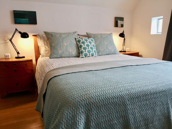 A neatly made bed with patterned pillows, a bedside lamp, and a clock on a wooden nightstand.