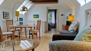 A cozy loft bedroom with a sloped ceiling, a dining area with wooden furniture, and a view through an open door. - Charming Renovated 19th-century Coach House (EDINBURGH)