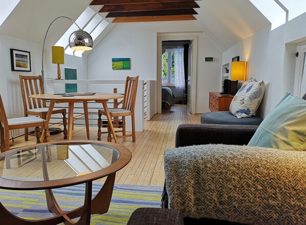 Une chambre à coucher confortable, aménagée en mezzanine avec un plafond en pente, un coin repas avec des meubles en bois et une vue dégagée grâce à une porte ouverte.
