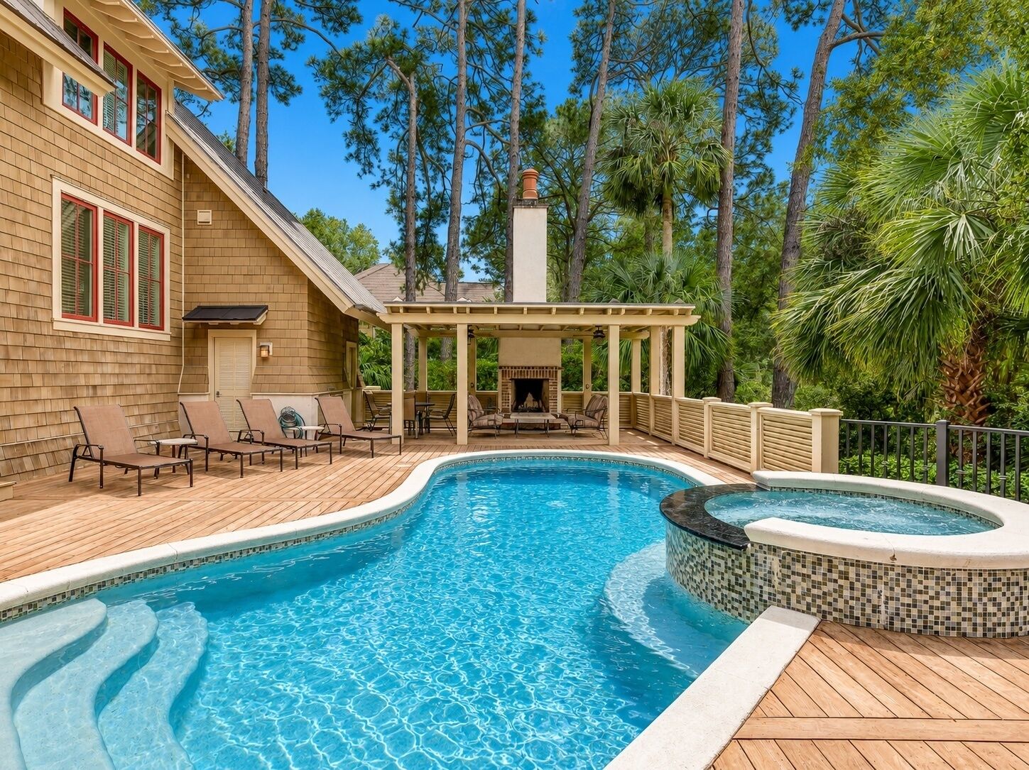 A swimming pool with a hot tub, deck chairs, and a covered seating area.