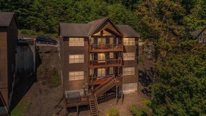 A multi-story wooden cabin with a balcony on the second floor, surrounded by dense forest. - Beautiful Lakefront Getaway - Sleeps 26 - Norris Lake’s Best Location (La Follette)