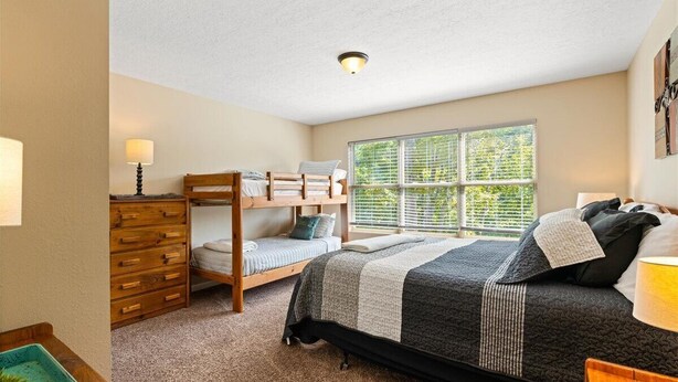 A bedroom with a bunk bed, a dresser, a bedside table, and a window with blinds.