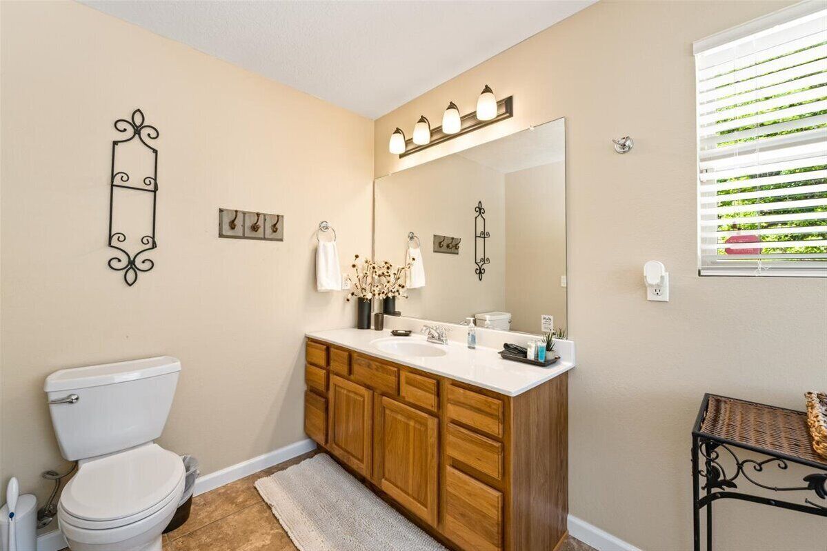 A bathroom with a toilet, wooden vanity, white sink, and a large mirror.