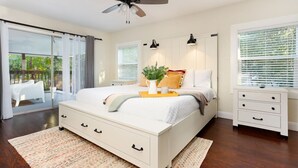 Een slaapkamer met een groot bed, nachtkastjes, een plafondventilator en uitzicht op de omgeving door een schuifdeur.