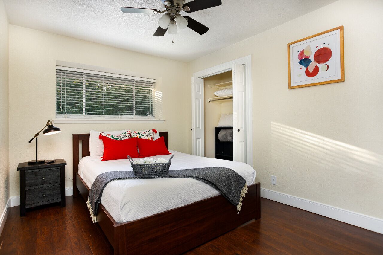 A bedroom with a bed, a nightstand, a ceiling fan, a window with blinds, and a door leading to a closet.