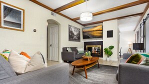 Een woonkamer met een open haard, grijze banken, een houten salontafel en een groot schilderij boven de haard.