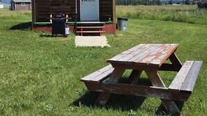 A wooden cabin with a picnic table in a grassy field, a door, and a window. - Vacation Cabin On 5 Acres With Pond . Sleeps 3 (kalispell)
