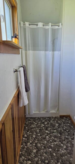 Une salle de bain avec un rideau de douche, un porte-serviettes avec des serviettes, un meuble-lavabo en bois et un sol à motifs de galets.