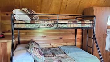 A bunk bed with a patterned bedspread, a wooden ceiling, and a chair with a woven seat.